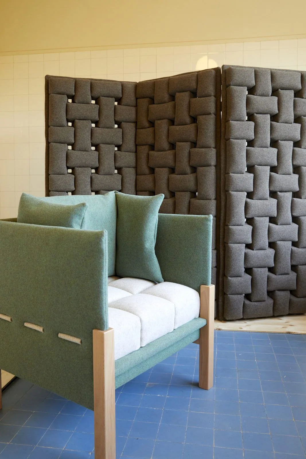 Le fauteuil acoustique GOUPIL, assise vert d'eau et piètement bois, devant des panneaux muraux matelassés.