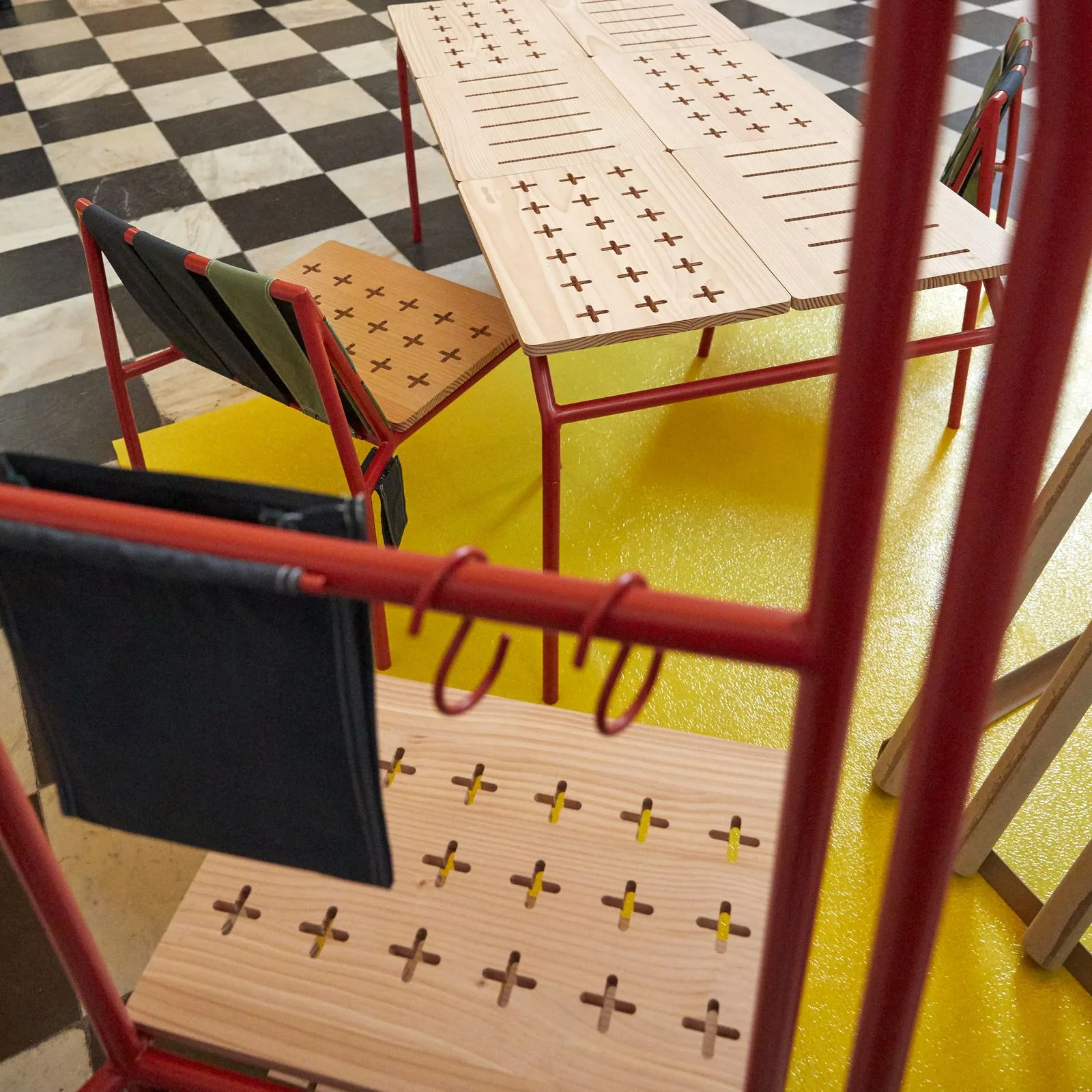 Table et chaises rouges de la ligne DE-TENTE, développée avec Cabanon, exposées sur un tapis jaune.