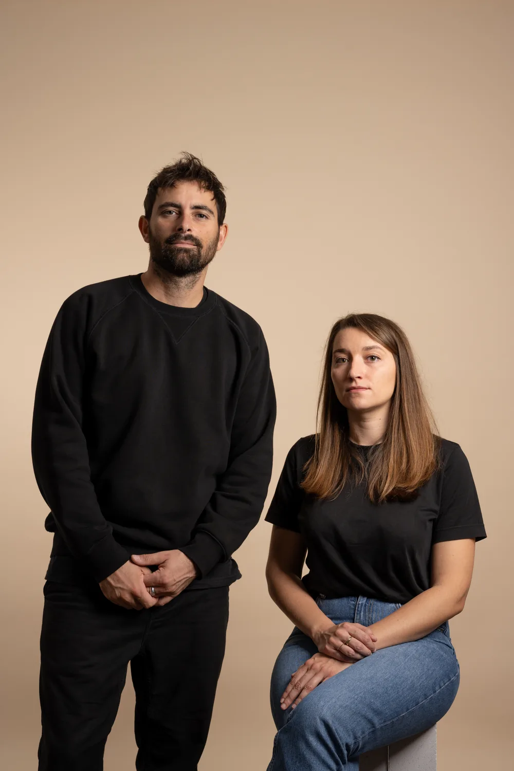 Luis Bellenger et Pauline Capdo, du studio paulineplusluis, vêtus de noir devant un fond sable uni.