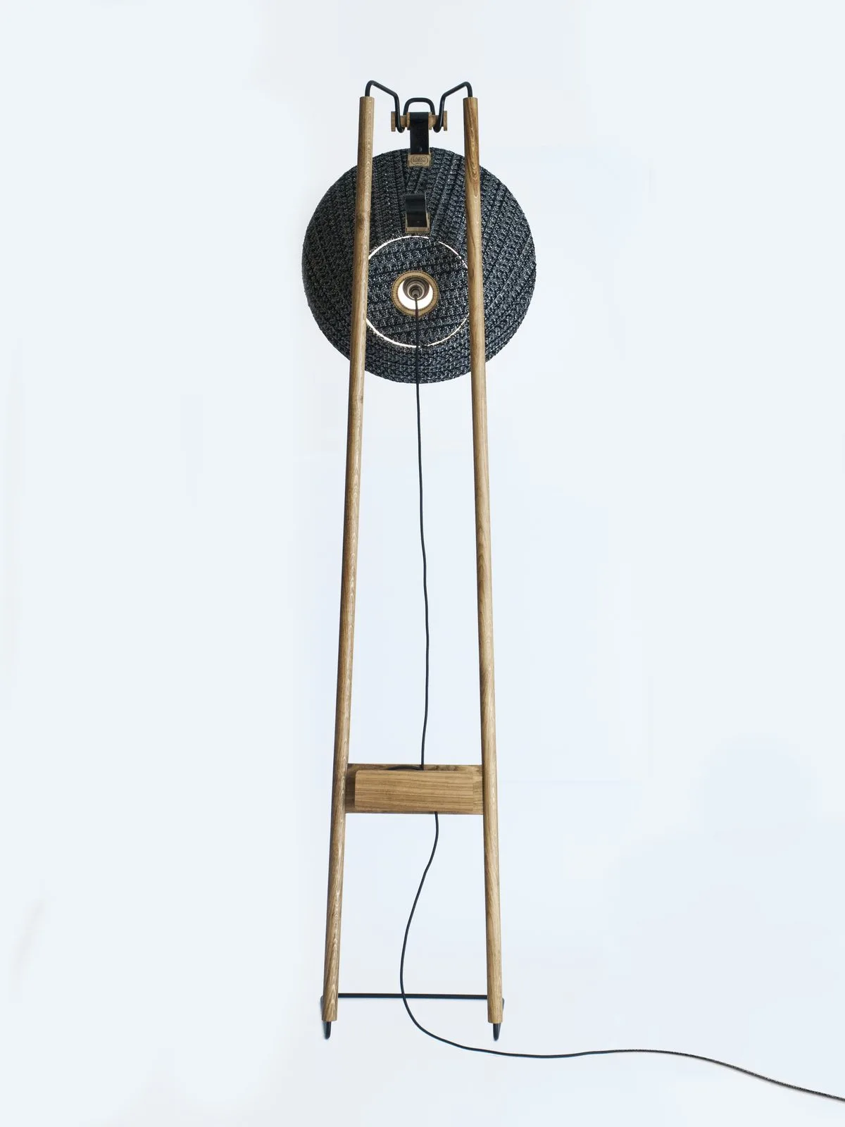 Lampadaire MASHÜT : un disque tressé sombre monté sur un piètement en bois clair.