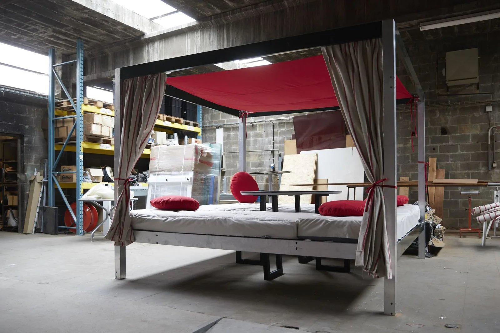 La structure COCOOZY montée dans l'atelier : cadre d'aluminium, toile rouge tendue en toiture, bains de soleil et coussins.