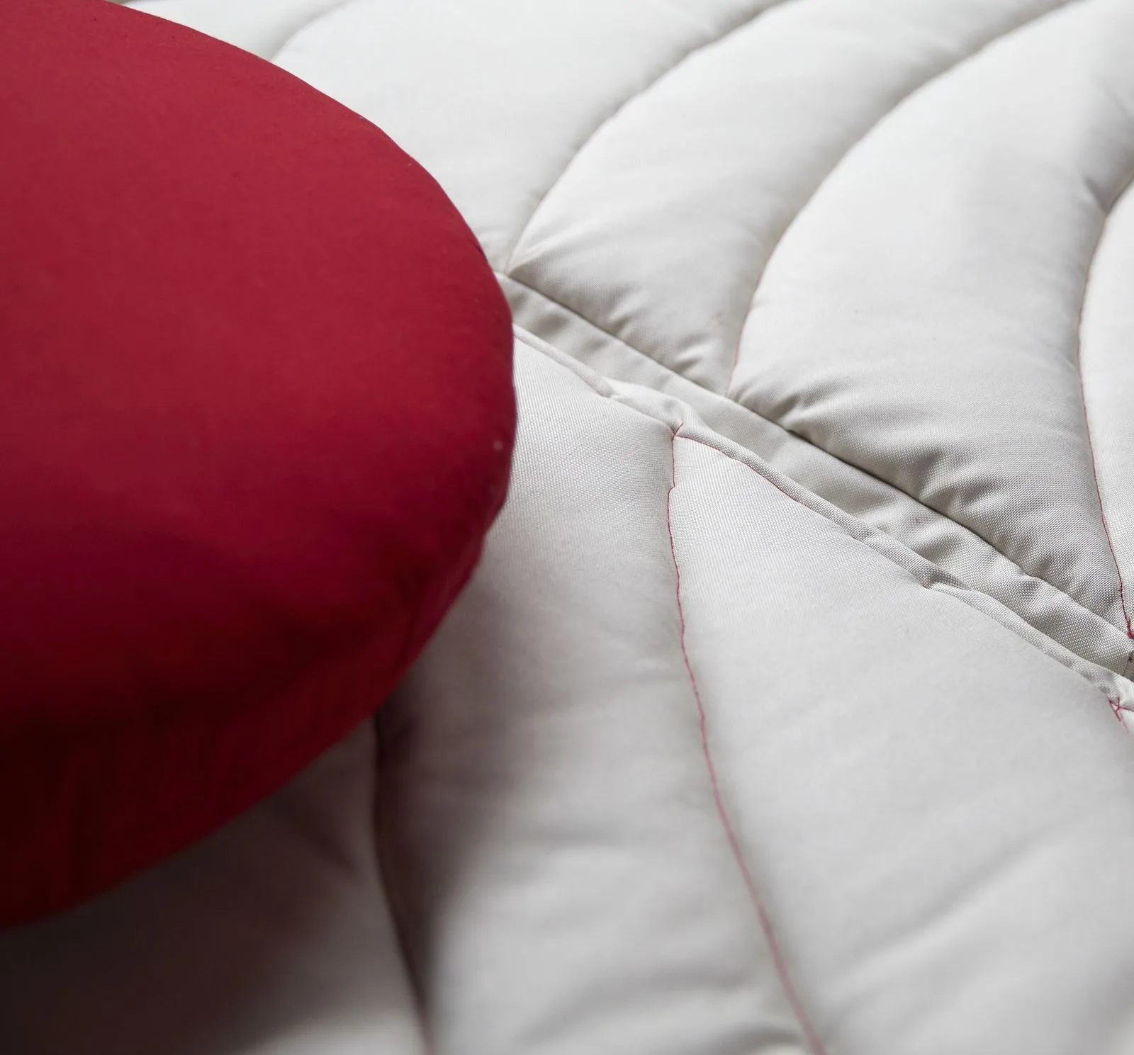 Gros plan sur un coussin rouge posé sur un matelas matelassé écru.