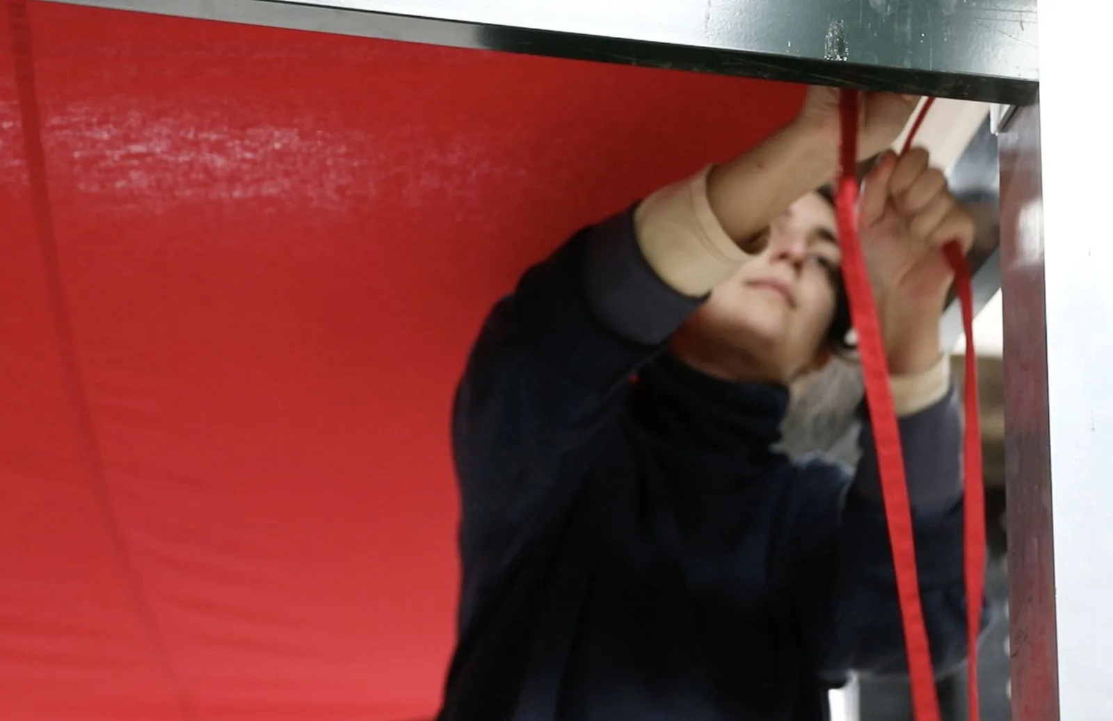 Une personne tend une sangle rouge sous la toile de la structure.