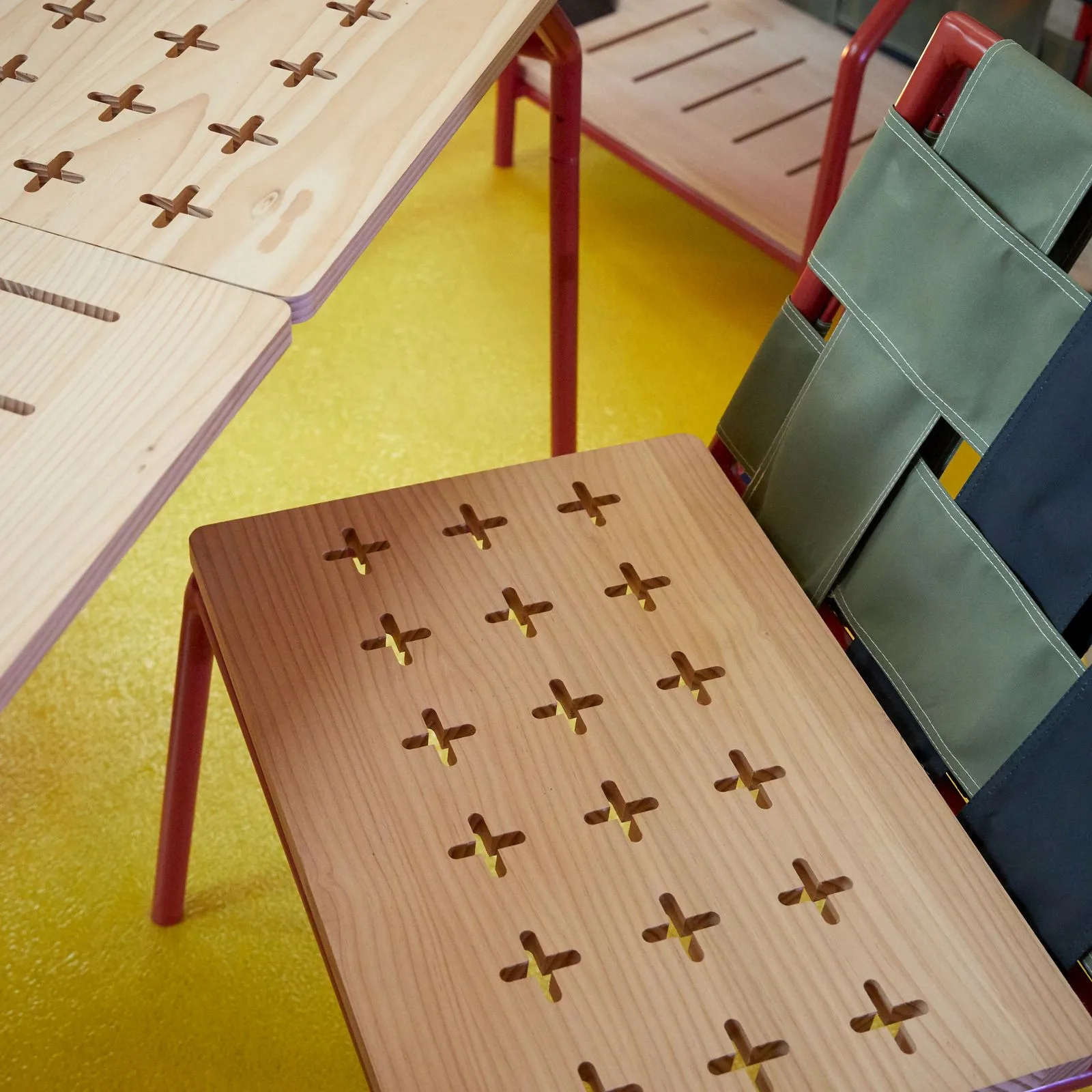 Détail du plateau de table ajouré de croix, et d'une assise à sangles vertes et noires.