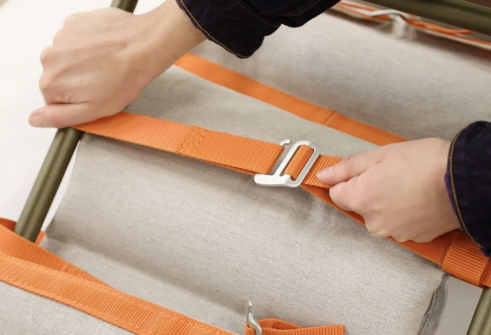 Deux mains engagent une sangle dans sa boucle métallique sur l'assise.