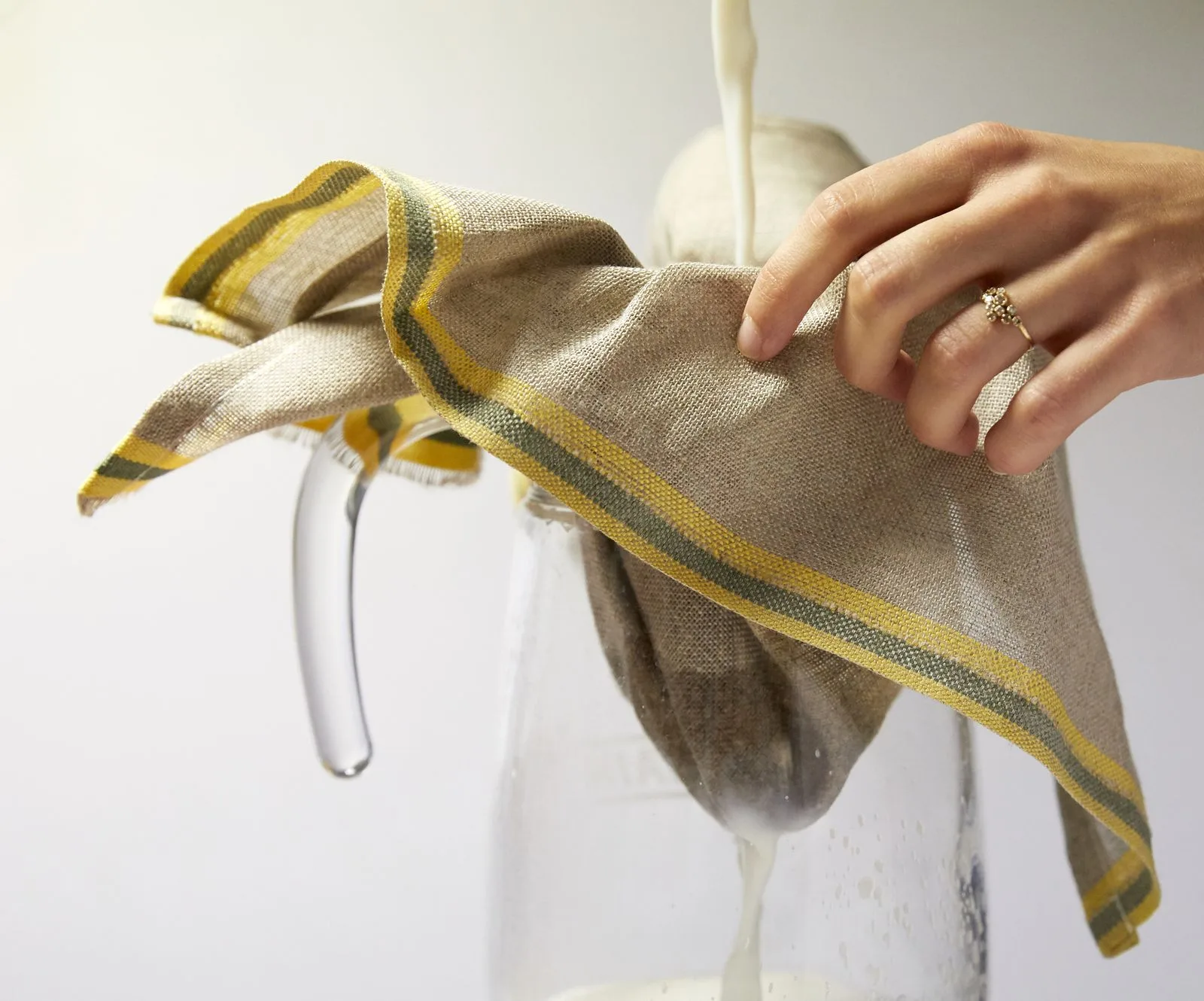 Contenant alimentaire en lin suspendu, ourlet jaune, tenu par une main.