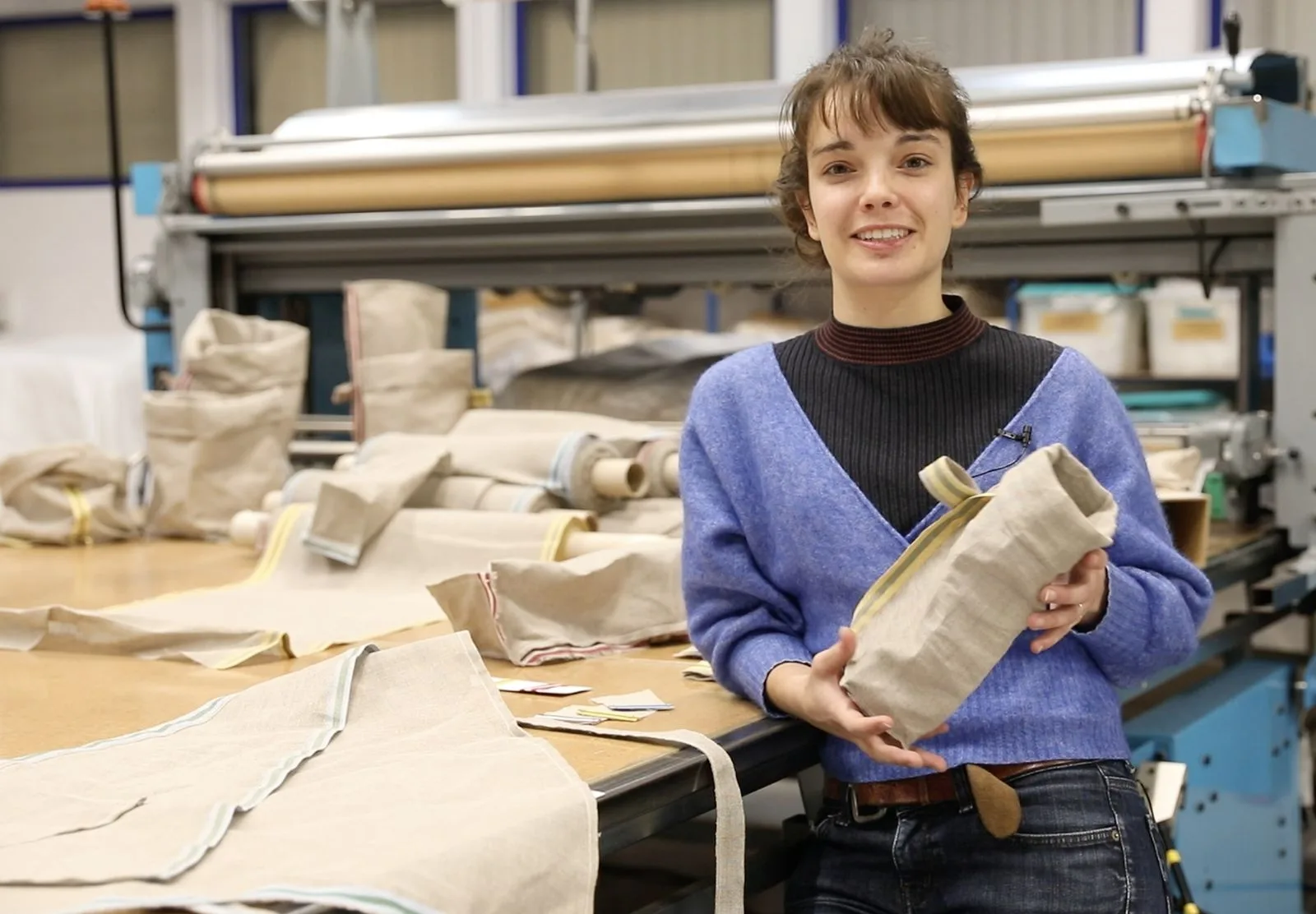 Maëlle Petitjean tient un contenant de la collection devant les métiers de l'atelier.