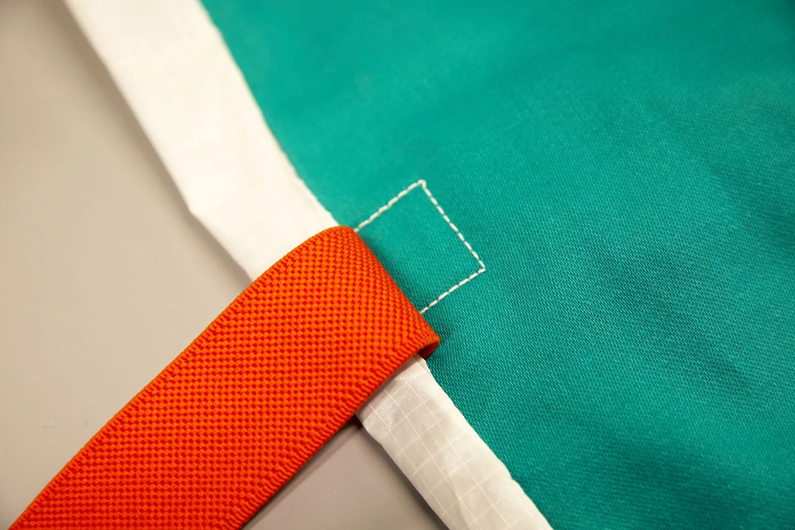 Détail d'une sangle orange cousue sur une toile vert d'eau.