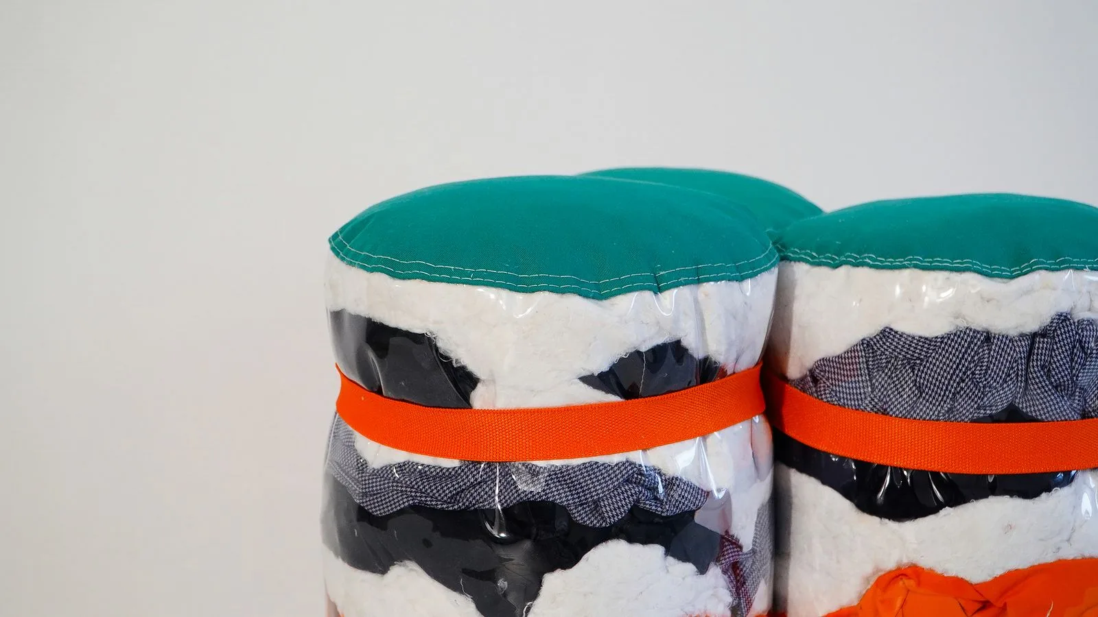 Plusieurs cylindres alignés, ceinturés d'une sangle orange, formant une banquette continue.