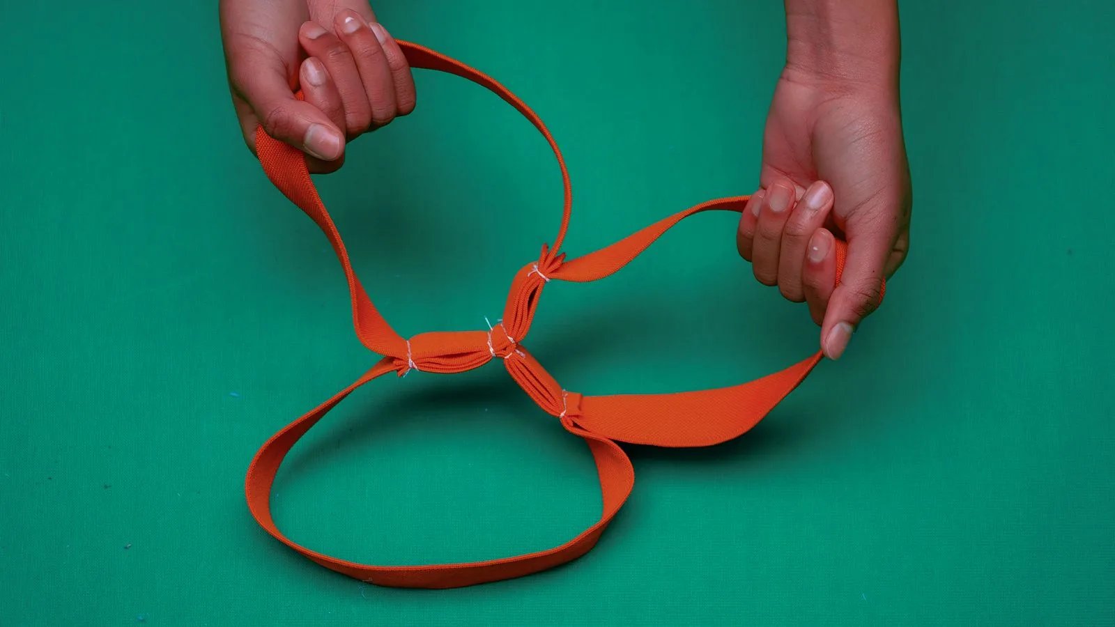 Deux mains tiennent une boucle de sangle orange sur fond vert.